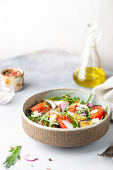 Eggplant salad with tomatoes, arugula and feta cheese in a bowl on white background