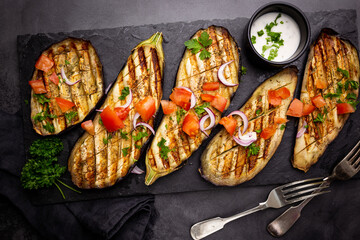 Grilled eggplant slices, garnished with fresh herbs, on black background, top view