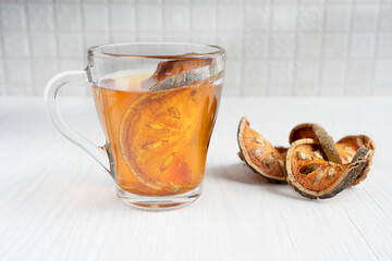 Traditional healing asian matoom tea made of dried bael fruit slices, also known as wood apple, in transparent glass cup on white wooden background at kitchen. Image with selective focus