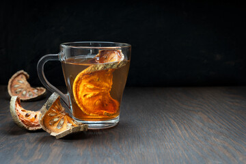 Thai beneficial matoom tea made of dried bael fruit slices, also known as wood apple, in transparent glass cup on dark brown wooden table at kitchen. Image with selective focus and copy space