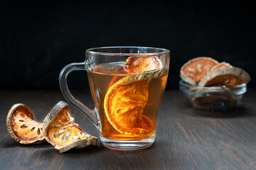 Thai traditional matoom tea made of dried bael fruit slices, also known as stone apple, in a transparent glass cup on dark brown wooden background at kitchen. Image with selective focus