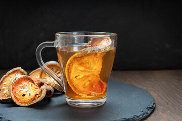Thai traditional healing matoom tea made of dried bael fruit slices, also known as stone apple, in transparent glass cup on stony tray on dark wooden table. Image with selective focus and copy space