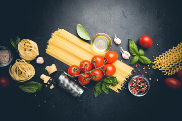 Pasta background. Several types of dry pasta with vegetables and herbs on black background. Free space for text. Top view