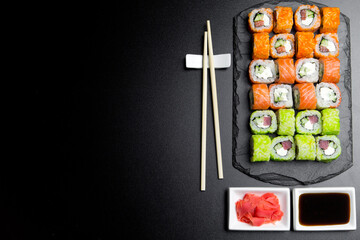 Sushi set served on a stone slate on a dark background. Sushi rolls with salmon, tuna, cucumber, wasabi, soy sauce and ginger. Sushi rolls photo for menu and advertising