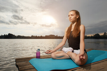 Close-up of a young girl doing yoga outdoors near a lake meditating in the Lotus position