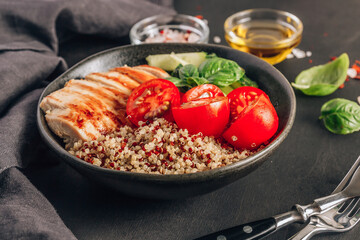 Healthy salad bowl with quinoa, tomatoes, chicken, cucumber and basil on black wooden background. Superfoods.