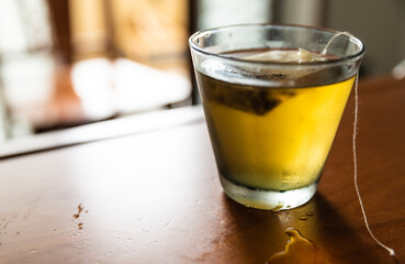 Close-up image of a cold herbal tea: the glass is covered with condensation. The sachet is infused in the glass.