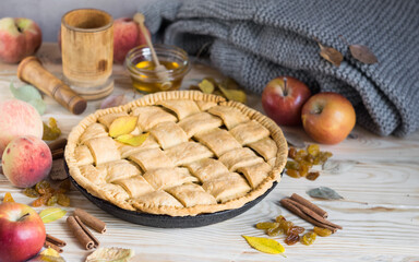 Homemade apple pie with ripe apples, peaches, species and autumn leaves on light rustic wooden background, horizontal orientation, selective focus