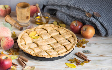 Homemade apple pie with ripe apples, peaches, species and autumn leaves on light rustic wooden...