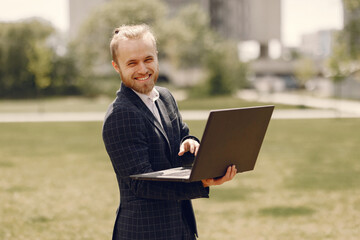 Businessman with laptop. Man in a black suit. Guy in a summer city.