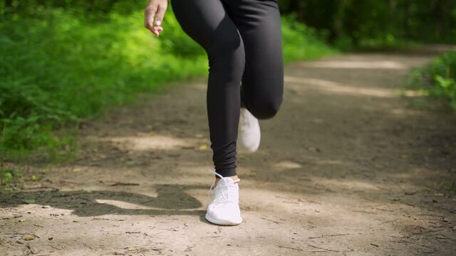 A woman ties her shoelaces while running through the woods