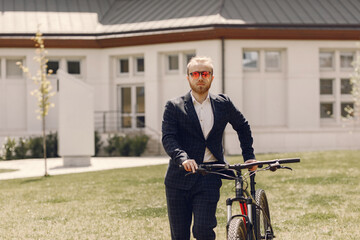 Fototapeta premium Businessman with bicycle. Man in a black suit. Guy in a summer city.