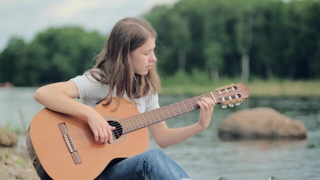 Young girl teaches to play the guitar in nature near a beautiful lake, hobby concept