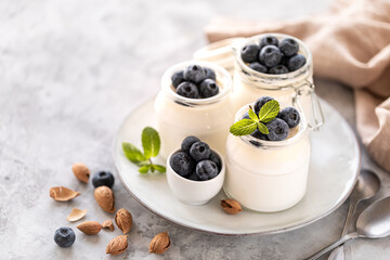 Non-dairy alternative. Vegetable yogurt in jars on a white background. Almond cream in a glass jar and fresh blueberry on a light plate and almond seeds. Healthy eating concept. Copy space for text