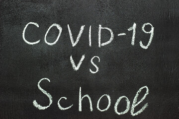 Fototapeta premium COVID-19 against school is written on a blackboard in white chalk.