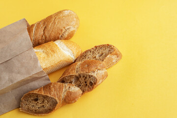 Fresh, flavorful baguettes made from rye and wheat flour, with sesame seeds, in a craft bag, and sliced pieces on a bright yellow background. Ecological concept of the crop. Top view, selective focus