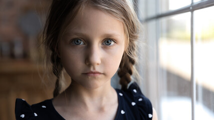Crop close up portrait of serious sad little Caucasian girl look at camera, unhappy small child kid...