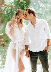 A beautiful bride and a young groom are standing near a window in a white studio. Wedding in the interior. Wedding portrait of newlyweds in love.