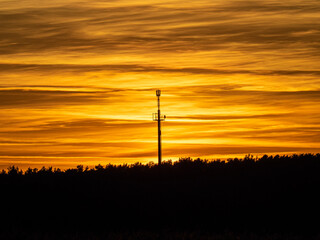Cell tower stands against orange colored sky at sunset