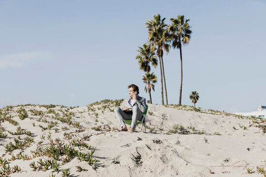 Businessman talking on smart phone on sunny beach, Los Angeles, California