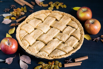 Apple pie with ripe apples, species and autumn leaves on dark wooden table, horizontal orientation,...