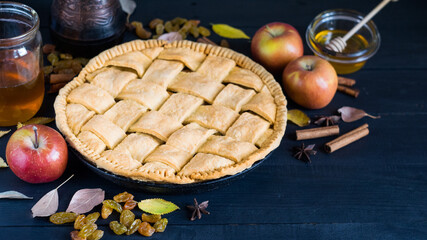 Homemade apple pie with ripe apples, species and autumn leaves on dark rustic wooden background, horizontal orientation, selective focus