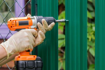 Work with a drill-screwdriver with an electric battery on a metal fence.
