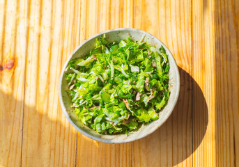 Greens and tuna salad in a ceramic bowl on a wooden table.
