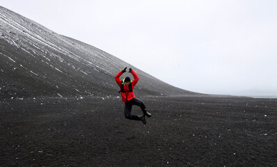Antarctica, deception island, man jumping in volcanic black landscape during snow storm