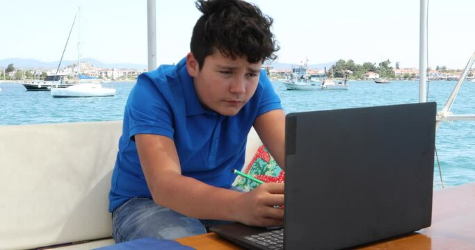 Teenage boy studying on yacht deck Online learning education distance learning for kids at home Homeschooling during quarantine or isolation