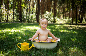 A scared little girl sits in a tub of water in nature and looks at the camera