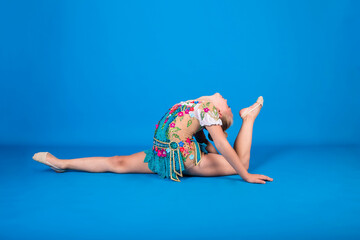 a beautiful female athlete in a gymnastic costume performs a longitudinal split with her leg raised...