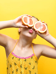 Summer happiness of a young woman with a grapefruit on a yellow background