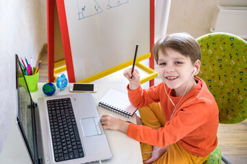 A boy sitting at a table at home in front of a laptop. Boy doing homework