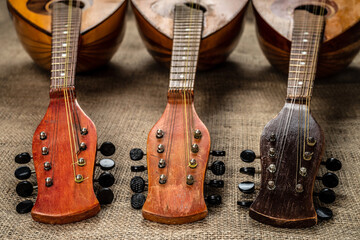 Three old mandolins rotated fingerboards to the camera. On a background of rough burlap texture.