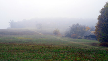 Fototapeta na wymiar Foggy autumn landscape with a road on a hill in the middle of a field with windmills and a wooden hut.
