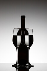 Beautiful bottle with two glasses with inverted reflection on white background