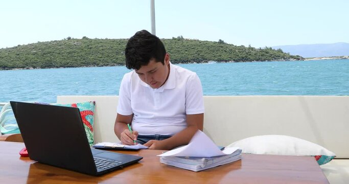 Teenage boy studying on yacht deck Online learning education distance learning for kids at home Homeschooling during quarantine or isolation