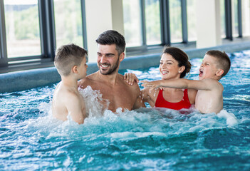 Smiling family of four having fun and relaxing in indoor swimming pool at hotel resort.