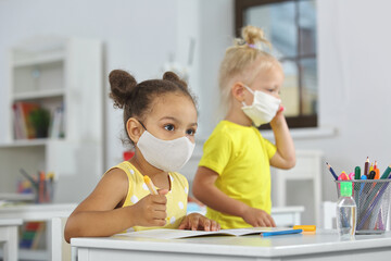 A dark-skinned girl with a medical mask listens attentively to the teacher