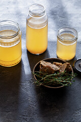 Glass jar with yellow fresh bone broth on dark gray background top view. Healthy low-calories food is rich in vitamins, collagen and anti-inflammatory amino acids