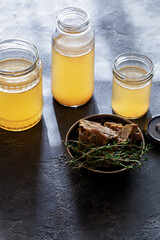 Glass jar with yellow fresh bone broth on dark gray background top view. Healthy low-calories food...