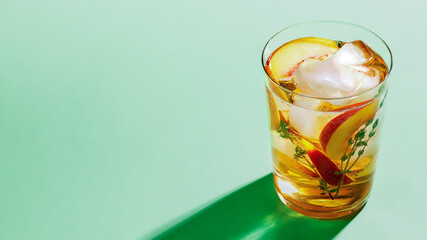 Sparkling cold brew peach tea with thyme in glass on green paper background close-up. Refreshing summer non-alcoholic drink concept