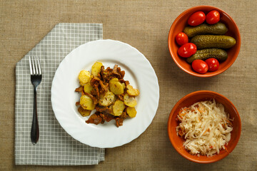 a plate of potatoes with larvae mushrooms on a napkin and a fork next to pickled cucumbers and tomatoes and cabbage.
