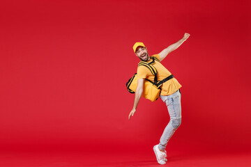 Fototapeta na wymiar Full length delivery employee man guy male 20s in yellow cap t-shirt uniform thermal food bag backpack work courier service during quarantine covid-19 virus, standing isolated on red background studio