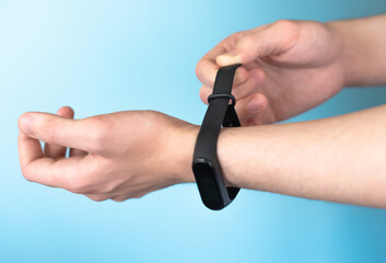 Close-up of the hands of a young man of European nationality, putting on a fitness bracelet. Concept of modern health monitoring technologies. Blue background, selective focus, copy space