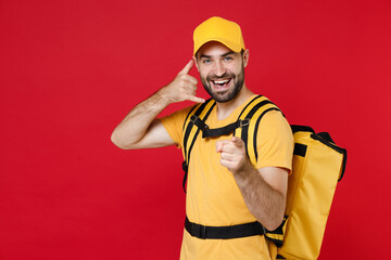 Delivery employee man guy male 20s in yellow cap t-shirt uniform thermal bag backpack with food work as courier isolated on red background studio. Service during quarantine coronavirus covid-19 virus.