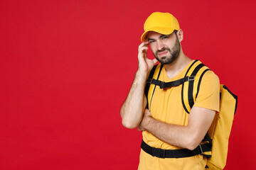 Sad delivery employee man guy 20s in yellow cap t-shirt uniform thermal bag backpack with food work as courier isolated on red background studio. Service during quarantine coronavirus covid-19 virus.