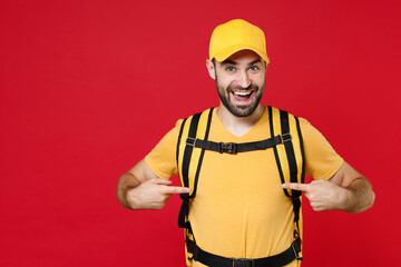 Delivery man 20s in yellow cap tshirt uniform thermal bag backpack points finger on shirt isolated on red background studio Guy male employee work as courier Service coronavirus covid-19 virus concept