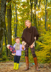 Fototapeta premium Happy mother with little son in autumn park. Autumn Family. Family parenthood and people concept - happy mother and little boy in autumn park. Happy family together in yellow nature.